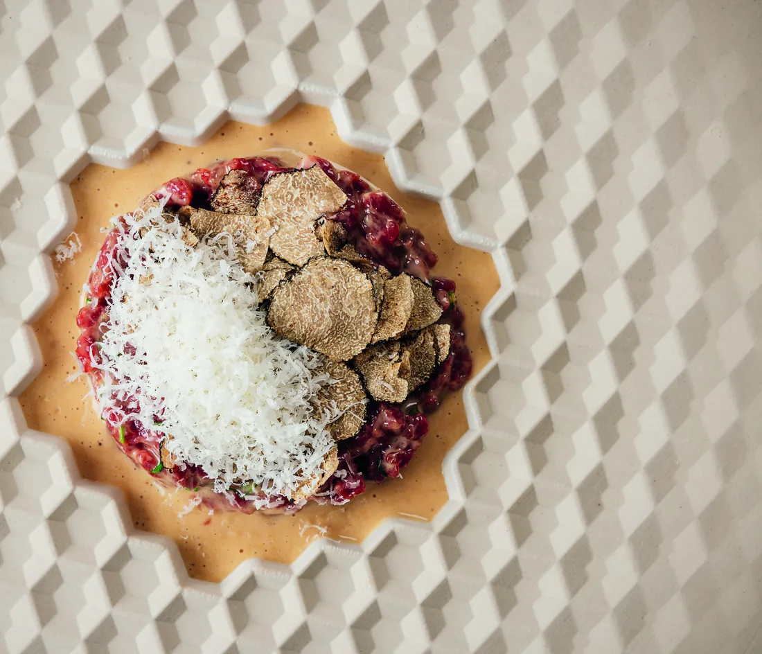 Beef tartare with shaved white truffle and grated parmesan on a sculpted white plate