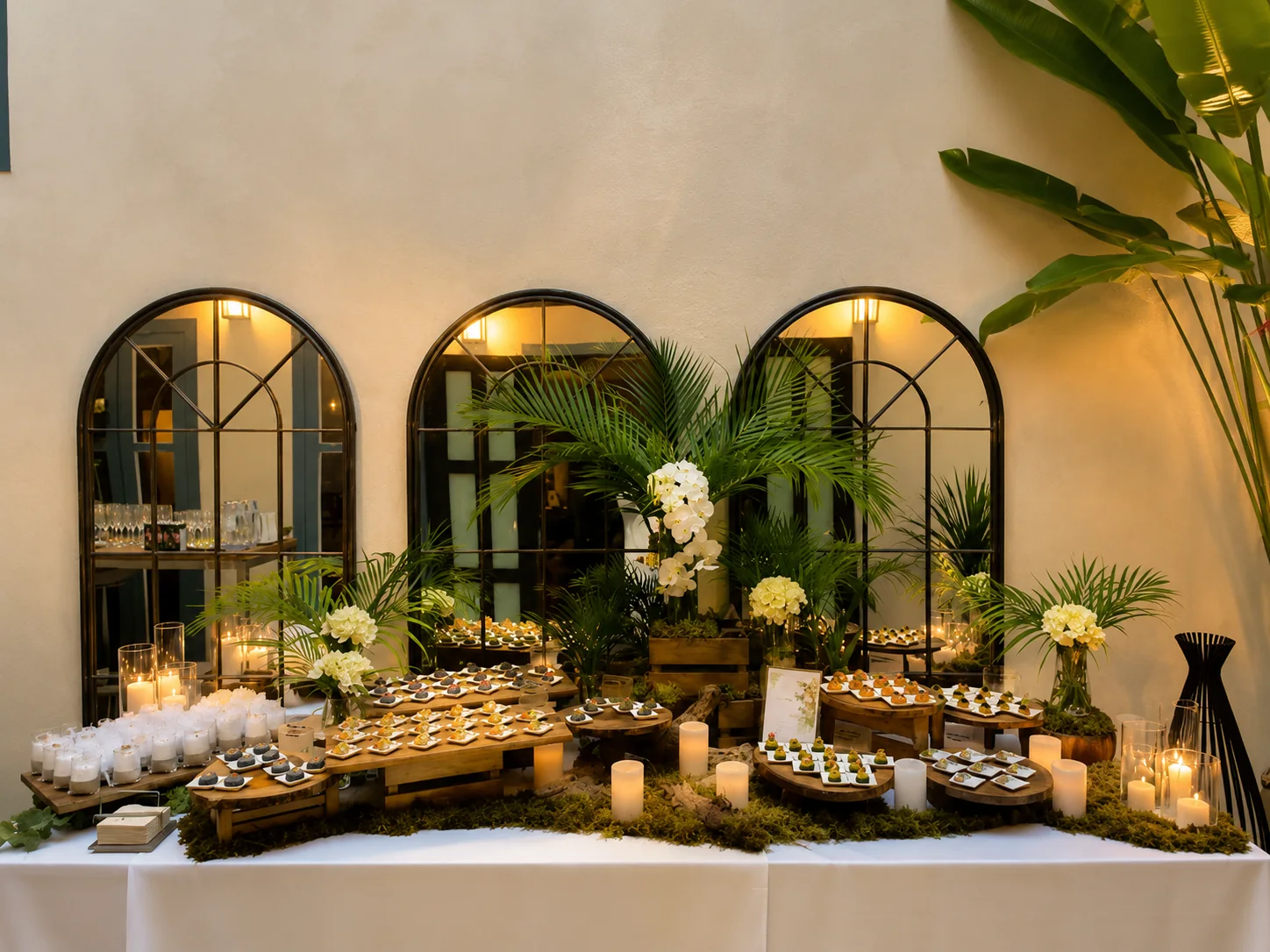 A canapé display built on tiered wooden stands with candles, moss and orchids, set for a reception