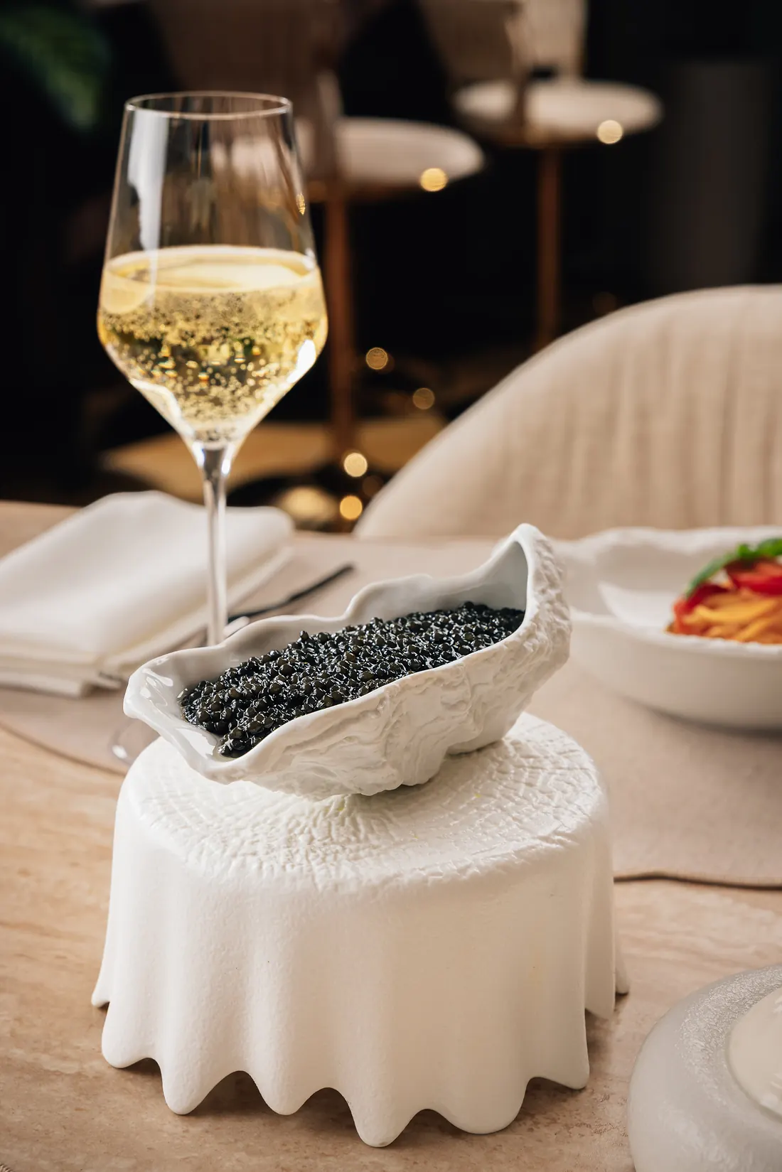 Caviar served on sculpted ceramic beside a glass of champagne in a darkened dining room