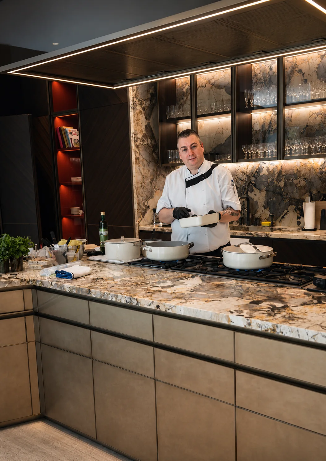 A chef in whites working at the stove of a marble residence kitchen, pans in service