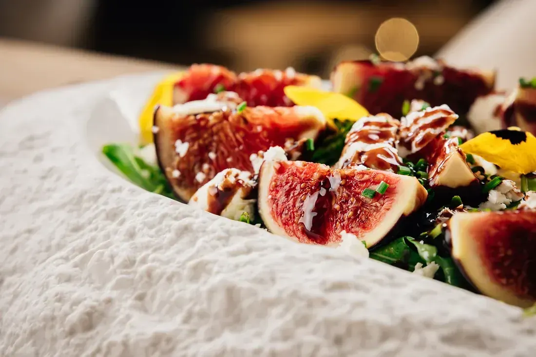 Fresh figs with goat’s cheese, rocket, chives and balsamic on a textured white plate