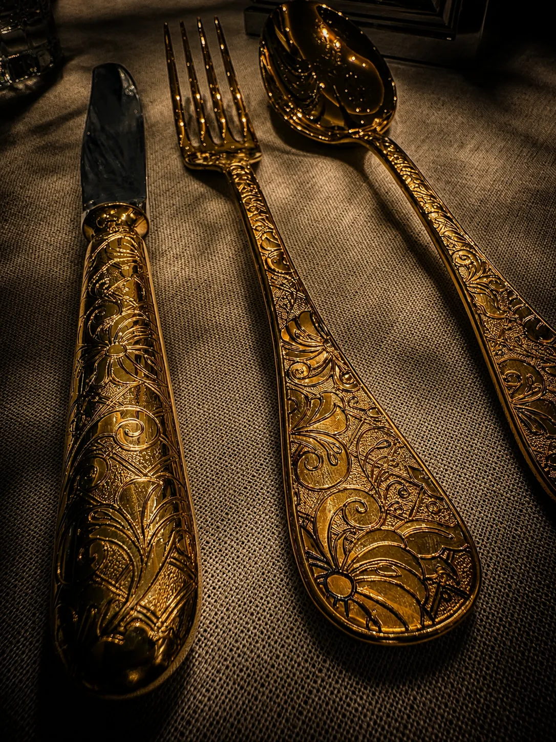 Twenty-four-carat gold-plated cutlery with engraved handles, laid on woven linen