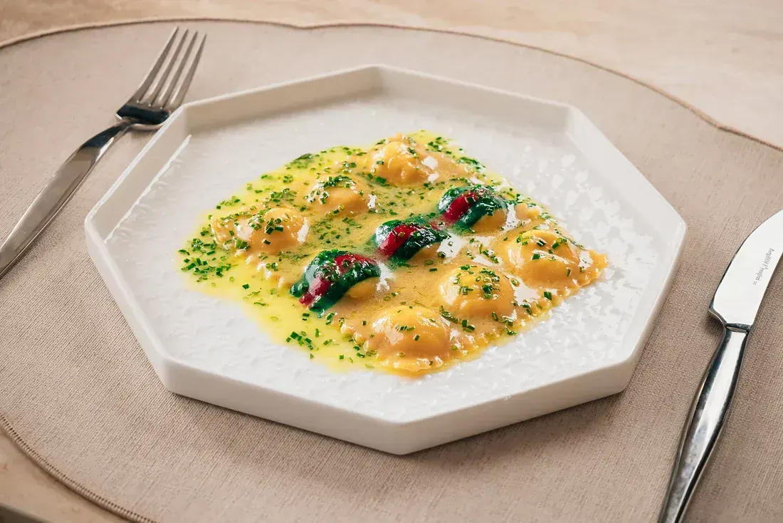 Handmade ravioli in butter sauce with chives, on an octagonal white plate