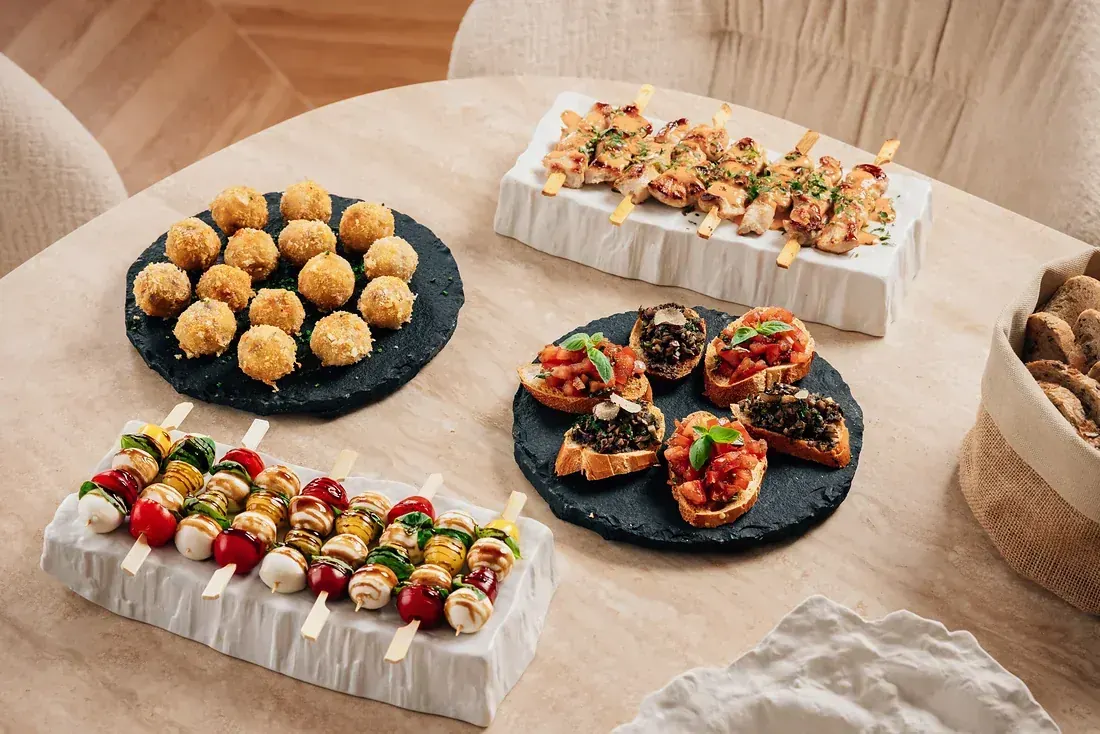 A canapé selection of arancini, chicken skewers, caprese skewers and bruschetta on slate and ceramic
