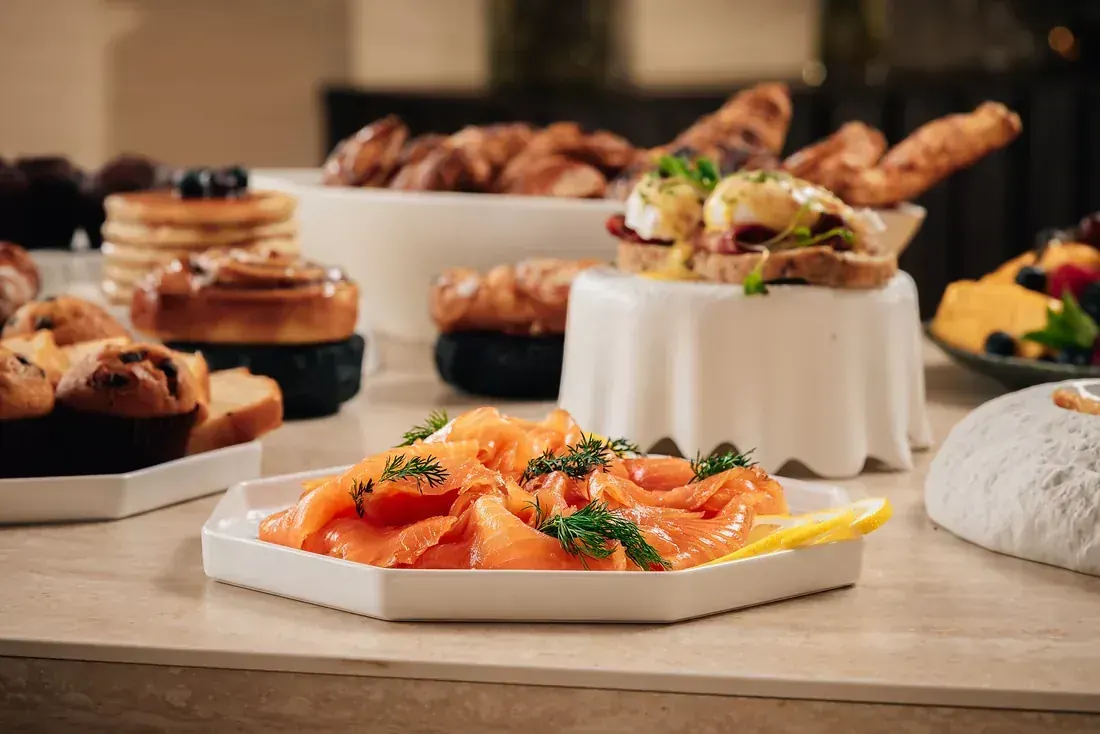 Smoked salmon with dill and lemon, with pastries and a breakfast spread behind
