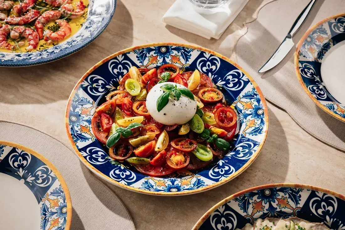 Burrata with heirloom tomatoes and basil on a majolica plate, seen from above