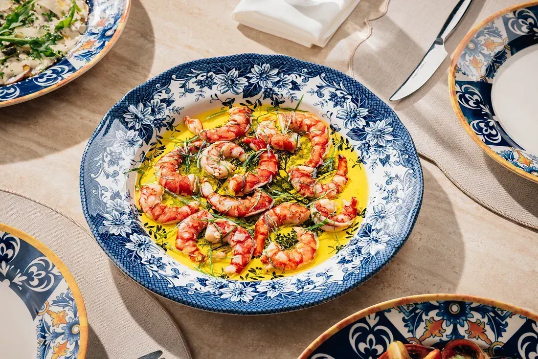 Red prawn crudo dressed in olive oil and herbs on a blue and white majolica plate