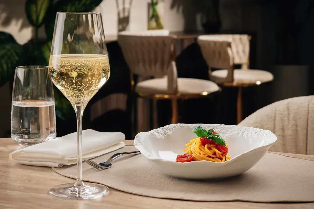 Spaghetti with tomato and basil in a sculpted white bowl, set with glassware in a private dining room
