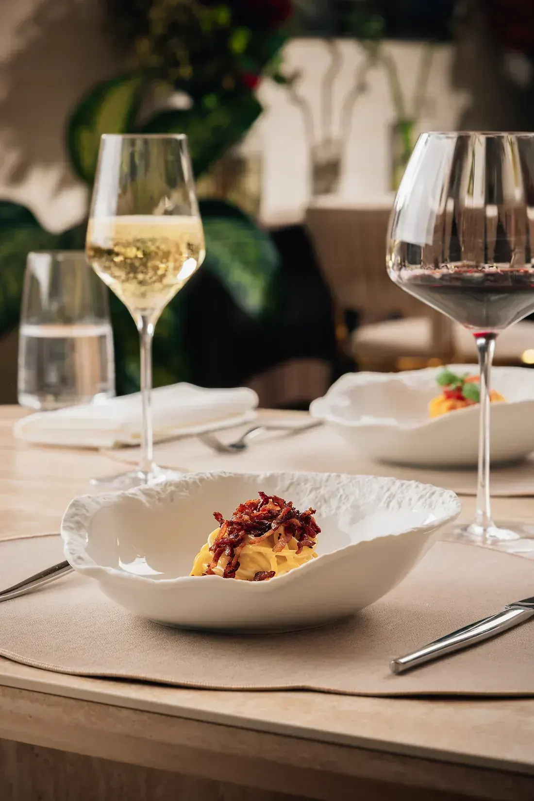 Tagliatelle topped with crisp guanciale, with white and red wine glasses behind