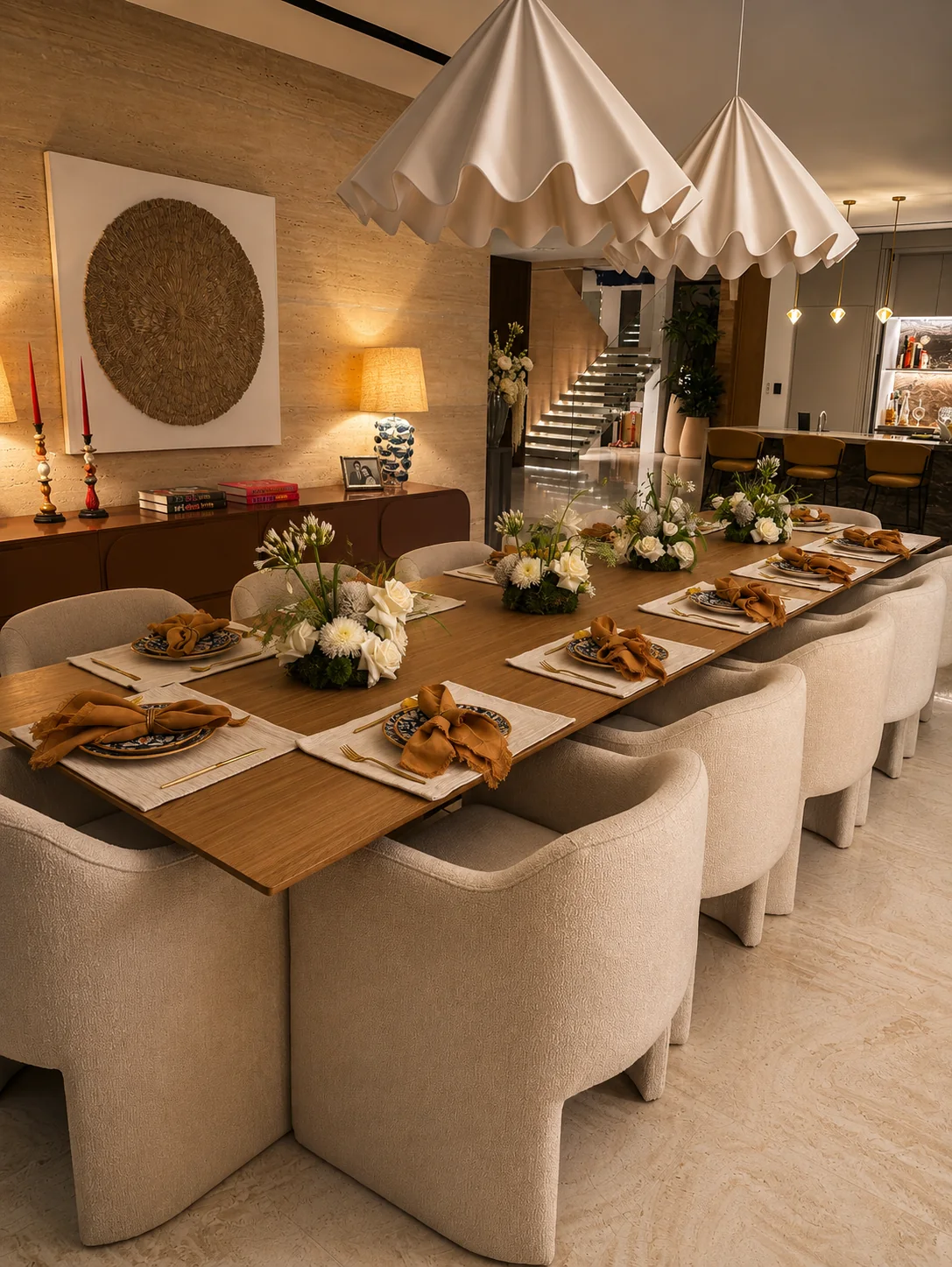 A villa dining room with a long table set for twelve beneath pleated pendant lights