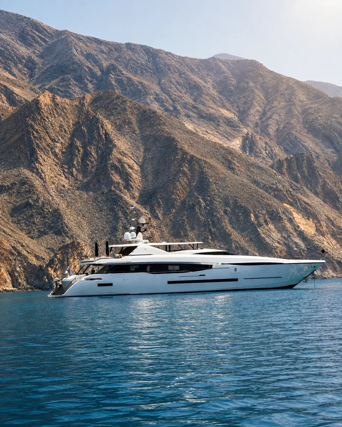 A white motor yacht at anchor in still water below dry mountains
